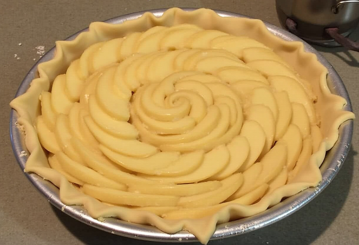 Apfelstücke in konzentrischen Kreisen auf dem Teig im Backblech für Französischen Apfelkuchen.
